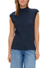 Marineblauwe mouwloze top van textuurstof, met een hoge hals en franjes. Gecombineerd met lichte denim wijde pijpenbroek.