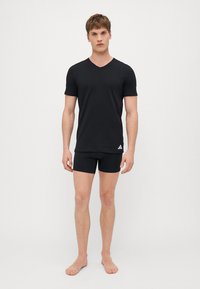 Schwarzes V-Ausschnitt-T-Shirt aus weichem Stoff, kombiniert mit passenden schwarzen Boxershorts. Das Shirt hat ein kleines weißes Logo-Detail.