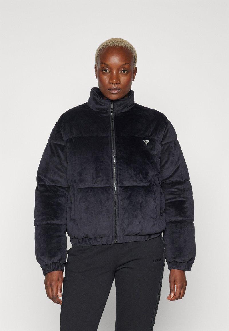 Giubbotto puffy nero in peluche con colletto alto, zip frontale completa e polsini elasticizzati. Presenta un piccolo logo triangolare sul petto.