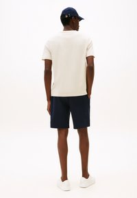 Meeste kreemjas t-särk, tumelõhk sinised lühikesed püksid ja valged tossud. T-särgil on ümara kaelusega krae, lühikestel pükstel on küljetaskud, üldine disain on vabaaja stiilis.