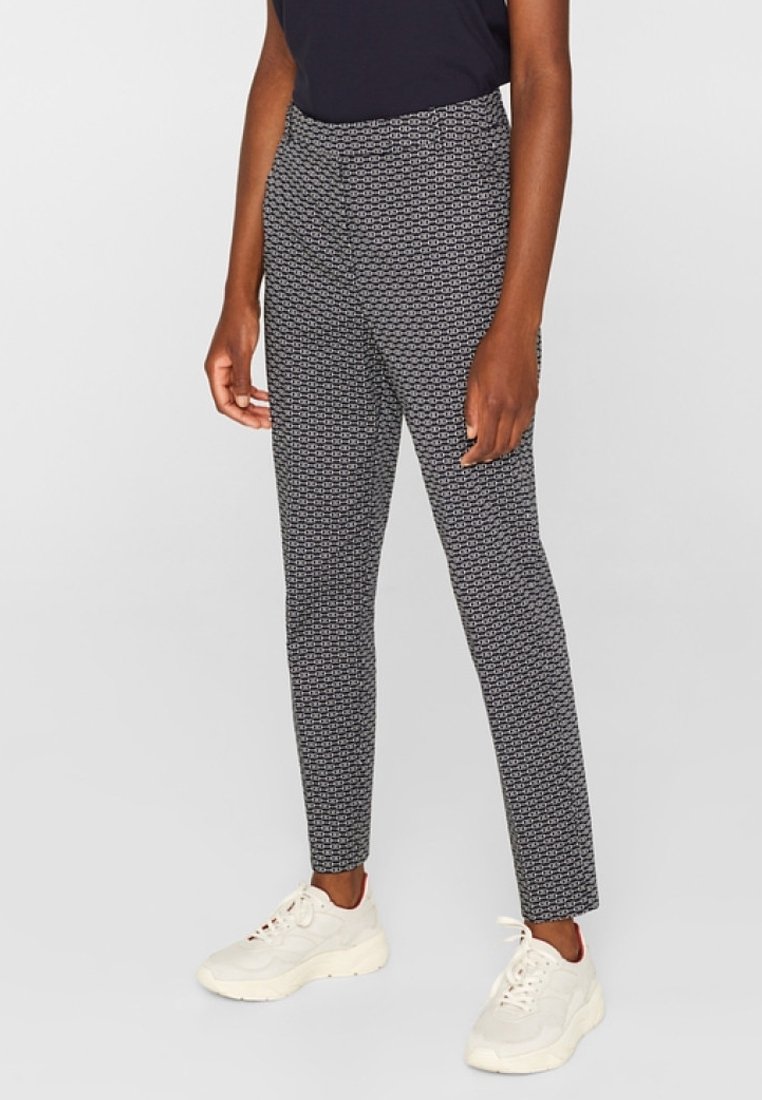 Pantalon noir et blanc à motifs, coupe slim avec une taille haute, fabriqué en tissu tissé. Associé à des chaussures de sport blanches.