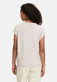Haut beige clair avec un motif texturé, manches courtes et un petit bouton décoratif à l'arrière. Tissu lisse avec une coupe décontractée.