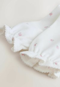 Fehér pamut ruha apró rózsaszín virágmintával. Bordázott ujjakkal, hullámos szegéllyel, puha textúrával és könnyű kialakítással rendelkezik.