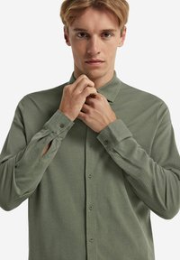 Långärmad grön skjorta med knappar i mjukt tyg, med krage, knappmanschetter och en subtil texturerad mönstring genom hela skjortan.