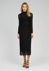 Robe noire avec de longues manches transparentes et un corsage ajusté. Le design présente un détail de tissu torsadé à la taille et une jupe fluide.