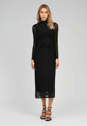 Robe noire avec de longues manches transparentes et un corsage ajusté. Le design présente un détail de tissu torsadé à la taille et une jupe fluide.
