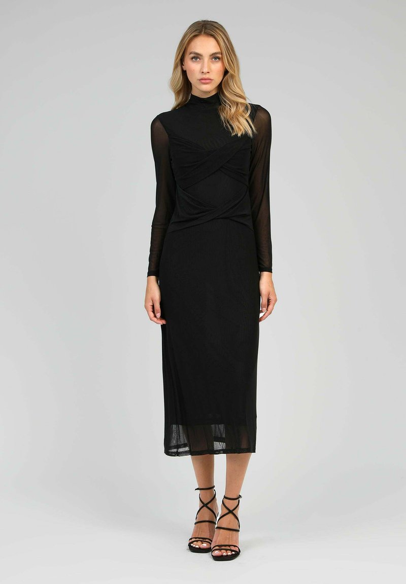 Robe noire avec de longues manches transparentes et un corsage ajusté. Le design présente un détail de tissu torsadé à la taille et une jupe fluide.