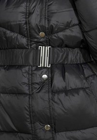 Černá péřová bunda s lesklou tkaninou, prošívaným designem a stříbrnými kovovými doplňky, včetně cvokového knoflíku a spony na pás.