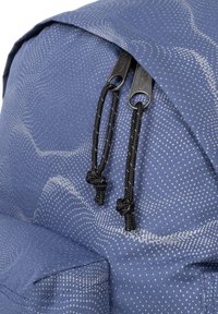 Sac à dos en tissu bleu avec un motif texturé, des tirettes de fermeture éclair noires doubles et des cordons de serrage noirs avec des extrémités nouées.