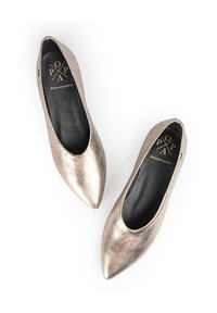 Bailarinas metálicas doradas con puntas afiladas, acabado suave y suelas negras con un logotipo. Textura suave, diseño minimalista.