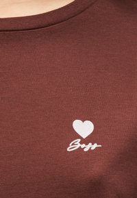 Καφέ T-shirt με υφασμάτινη υφή. Διαθέτει ένα λευκό γραφικό καρδιάς και τη λέξη "Bff" με καλλιγραφικά γράμματα. Σχεδίαση με στρογγυλή λαιμόκοψη.