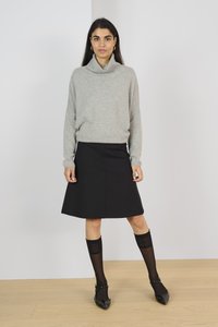 Pull en maille gris clair avec col roulé ; jupe noire évasée jusqu'aux genoux ; chaussettes noires à motifs montantes jusqu'aux genoux ; chaussures plates noires à bout pointu.