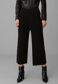 Svarta vida byxor i texturerat stickat tyg, med hög midja och en mjuk, elastisk midjeband. Kombinerat med blanka svarta ankelstövlar.