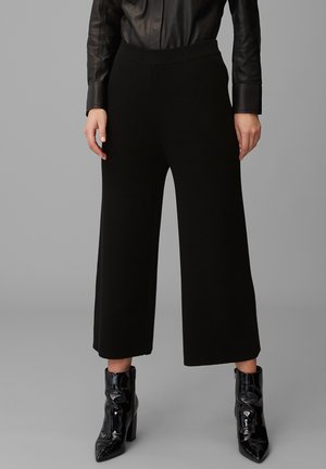 Pantaloni neri a gamba larga realizzati in un tessuto a maglia testurizzata, con vita alta e un cintura elastica liscia. Abbinati a stivaletti neri lucidi.