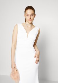Vestido branco ajustado com um decote em V profundo, com rendas nas ombreiras e uma textura suave. Acessorizado com uma clutch rosa fofinha e um colar de destaque.
