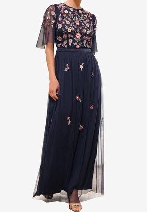 Maxikleid in Marineblau mit transparenten kurzen Ärmeln und floraler Stickerei auf dem Oberteil und Rock, kombiniert mit offenen Sandalen.