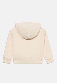 Sudadera cortada de color crema con mangas largas y puños acanalados, vista desde la parte trasera sobre un fondo blanco liso.