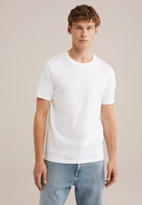 Camiseta de algodón blanca de manga corta con cuello redondo, textura suave, corte holgado, combinada con jeans de denim azul claro.