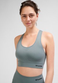 Stanik sportowy w miękkim szarym materiale, bezszwowy design, szerokie ramiączka, wspierający krój oraz czarny akcent z logo na pasie.