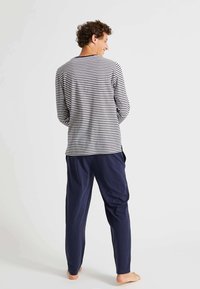 Haut à manches longues, rayé en blanc et marine, avec un col ras du cou. Associé à un pantalon marine ample, vu de dos.