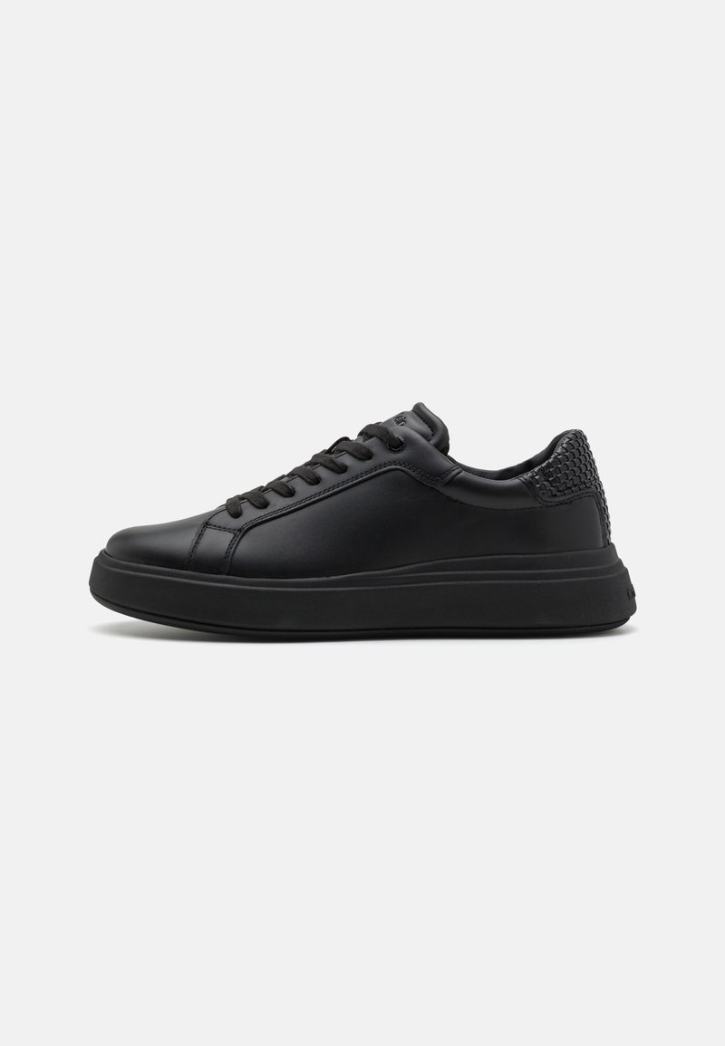 Baskets basses en cuir noir avec fermeture à lacets à l’avant et détail texturé au talon, vues de côté sur un fond clair uni.
