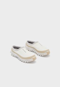 Baltos slip-on sportbačiai su tekstūruota medžiaga, rusvos spalvos akcentais ir išskirtiniu nelygiais padu. Turintys žemą profilį ir elastingą apykaklę.