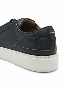 Black leather sneaker with textured finish, white rubber sole, minimalistic design, and subtle metal accent on the heel.