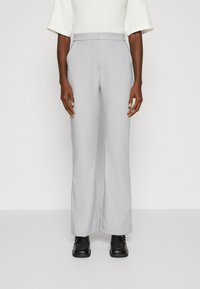 Světlé šedé kalhoty širokého střihu z texturované látky. Mají pas s poutky na pásek a přední sklady, v kombinaci s černými botami.