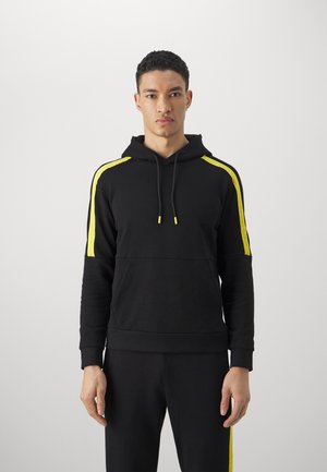Felpa nera con strisce gialle sulle maniche, cappuccio con cordino e polsini a coste. Tessuto liscio con un design aderente. Pantaloni neri coordinati.