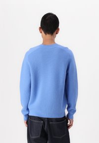 Svetlo modra pulover iz mehkega blaga, z okroglim izrezom, rebrastimi manšetami in sproščenim krojem, nosi se z temno denim hlačami.