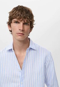Camicia a righe blu chiaro e bianca con bottoni, realizzata in un tessuto liscio, con colletto classico e vestibilità rilassata. Leggera lucentezza nella texture.