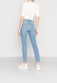 Světle modré úzké džíny s vysokým pasem, dvěma zadními kapsami a světle béžovou etiketu na pasu, doplněné bílými teniskami.