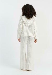 Felpa bianca lavorata a maglia con cappuccio e motivo a trame aperte, abbinata a pantaloni a gamba larga a righe con una finitura testurizzata.