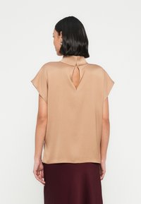 Beige lyhythihainen paita, jossa korkea kaulus ja takana avonainen yksityiskohta. Sileä kangas ja rento istuvuus, yhdistetty burgundinväriseen hameeseen.