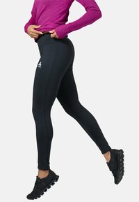 Zwarte, nauwsluitende legging met hoge taille en logodetail, gemaakt van rekbaar materiaal. Gecombineerd met een gestructureerde paarse lange mouw top.