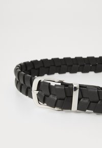 Cinturón de cuero trenzado negro con hebilla de metal plateado. El diseño presenta un patrón trenzado texturizado con bordes suaves.