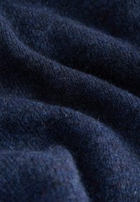 Dunkelblauer gestrickter Stoff mit weicher, flauschiger Textur sowie sichtbaren Schlaufen und Fasern in einem gefalteten, gewellten Muster.