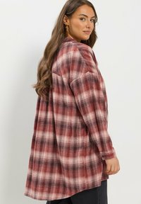 Czerwona i czarna koszula z flaneli w kratę, o luźnym kroju, z długimi rękawami i zaokrąglonym dołem. Teksturowany materiał o miękkim, ciepłym wyglądzie.