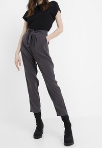 Czarny t-shirt z krótkim rękawem połączony z szarymi, dopasowanymi spodniami o wysokim stanie z paskiem i bocznymi kieszeniami. Modelka nosi czarne botki na obcasie.