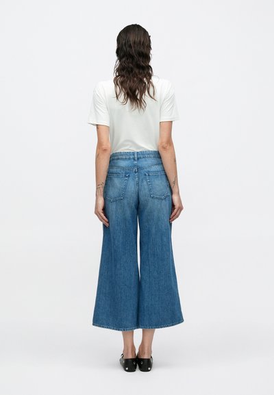 Παντελόνι τζιν με φαρδιά μπατζάκια σε ανοιχτό χρώμα, με ψηλή μέση, διαθέτει δύο πίσω τσέπες και ακατέργαστο τελείωμα. Συνδυασμένο με απλό λευκό μπλουζάκι.