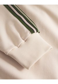 Light beige sweatshirt fabric with a ribbed cuff. Features a vertically striped accent in dark green and black with white. Smooth texture.