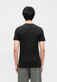 Črna bombažna majica s kratkimi rokavi in okroglim izrezom, prikazana od zadaj, z gladko teksturo in minimalističnim dizajnom.