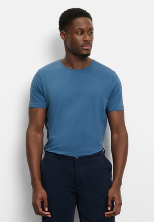 Blaues Baumwoll-T-Shirt mit rundem Ausschnitt und kurzen Ärmeln, kombiniert mit dunkler Hose. Glatte Textur, tailliertes Design.