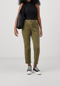 Olive green cargo pants with zippers at the ankles, paired with a black ribbed halter top and black and white lace-up sneakers. Black bag.