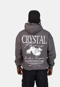 Szara, krótka bluza z kapturem z dużym białym nadrukiem z tyłu, który zawiera tekst "CRYSTAL Paris" oraz grafiki diamentów.