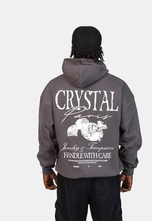 Szara, krótka bluza z kapturem z dużym białym nadrukiem z tyłu, który zawiera tekst "CRYSTAL Paris" oraz grafiki diamentów.