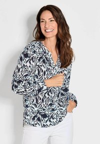 Blusa a maniche lunghe con motivo astratto blu e bianco, scollatura a V e orlo curvo. Realizzata in tessuto leggero e testurizzato.