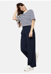 Striped navy and white cropped t-shirt paired with high-waisted, wide-leg navy trousers, completed with white and gold sneakers.