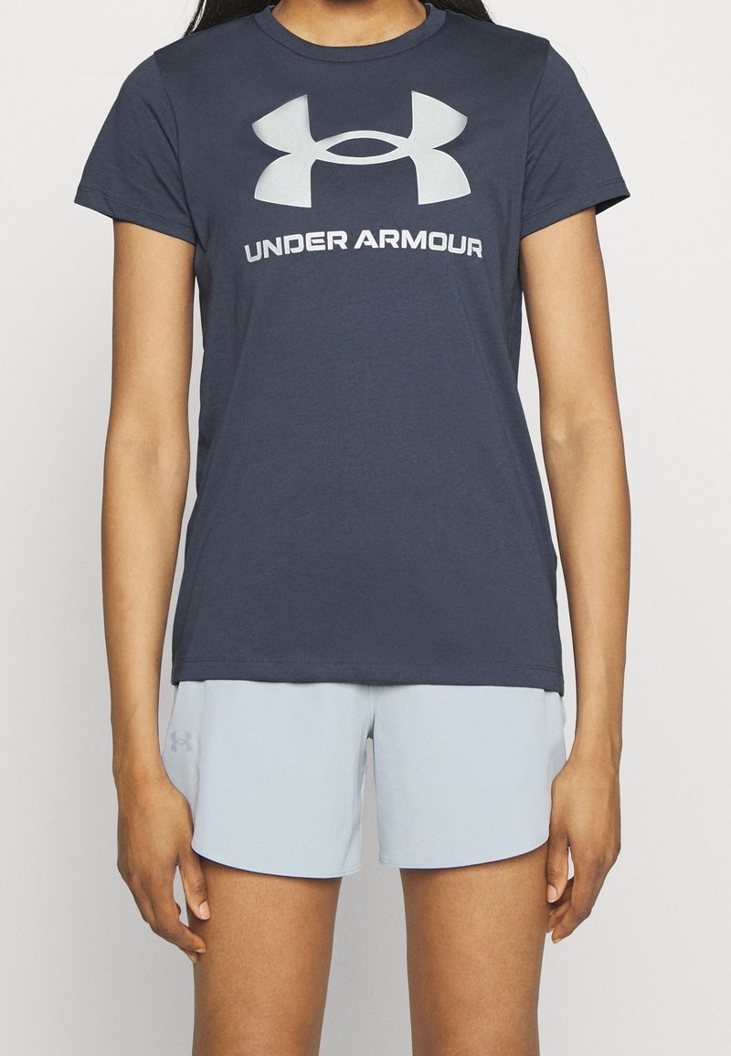 Mörk marinblå t-shirt med kort ärm och en stor ljusgrå "Under Armour"-logotyp på framsidan. Matchas med ljusblå shorts. Slät textur.