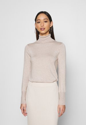 Pull en maille douce couleur beige, au design ajusté, avec des manches longues, associé à une jupe côtelée assortie, sur un fond neutre.